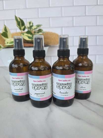 Four amber glass spray bottles labeled 'lip balm spray' by Lip Balm Co., arranged on a light marble surface with a white tile wall and a plant in the background.